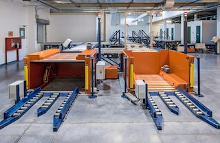 Hidrauliskas pacelšanas platformas paceļ preces no grīdas līmeņa līdz palešu transportēšanas konveijera augstumam Hidrauliskas pacelšanas platformas paceļ preces no grīdas līmeņa līdz palešu transportēšanas konveijera augstumam